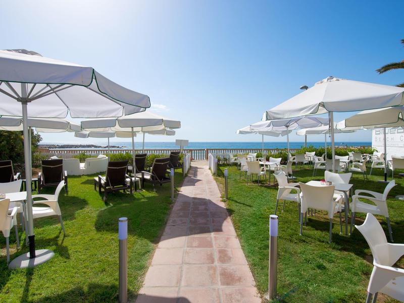 Terrasse ensoleillée avec tables, chaises et parasols blancs avec vue sur la mer.