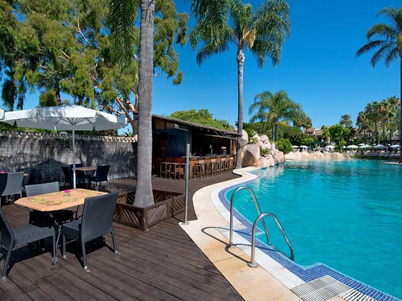 Espace lounge avec sièges près d'une grande piscine accueillante avec des palmiers.