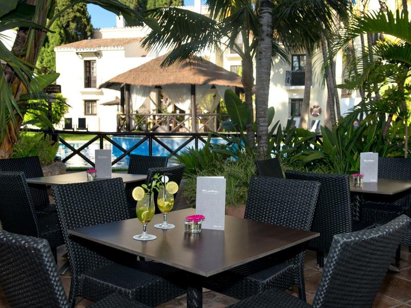 Espace extérieur confortable avec tables, chaises et parasol dans un jardin d'hôtel tropical.