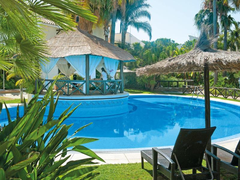Piscine ronde avec chaises longues et parasols dans un jardin tropical