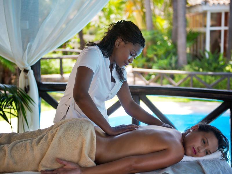 Femme recevant un massage sur une table près d'une piscine en cadre tropical.