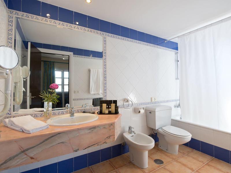 Salle de bain lumineuse avec murs carrelés bleu et blanc, lavabo, WC et grande douche.