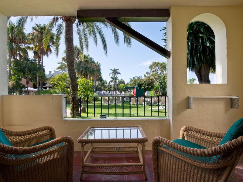 Balcon avec deux fauteuils en osier donnant sur un jardin avec palmiers et coin salon.
