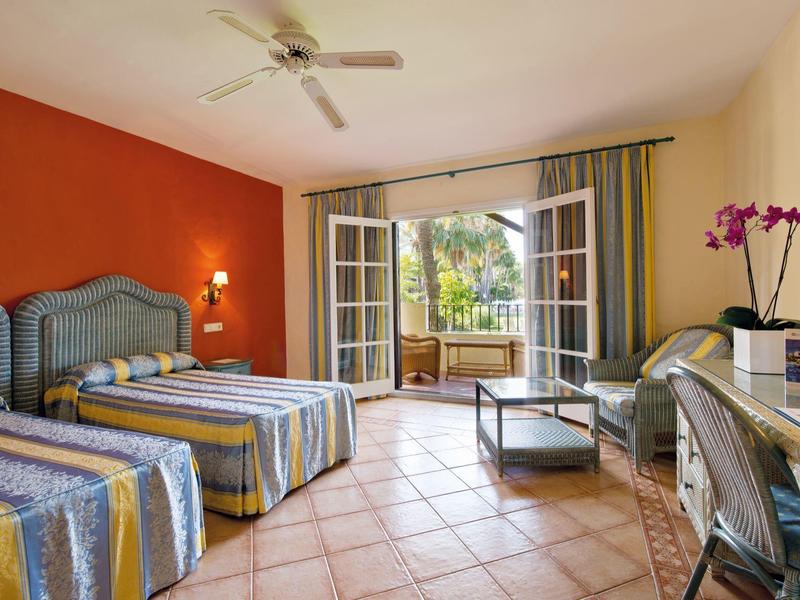 Chambre avec deux lits, porte moustiquaire vers la terrasse, vue sur un jardin tropical.