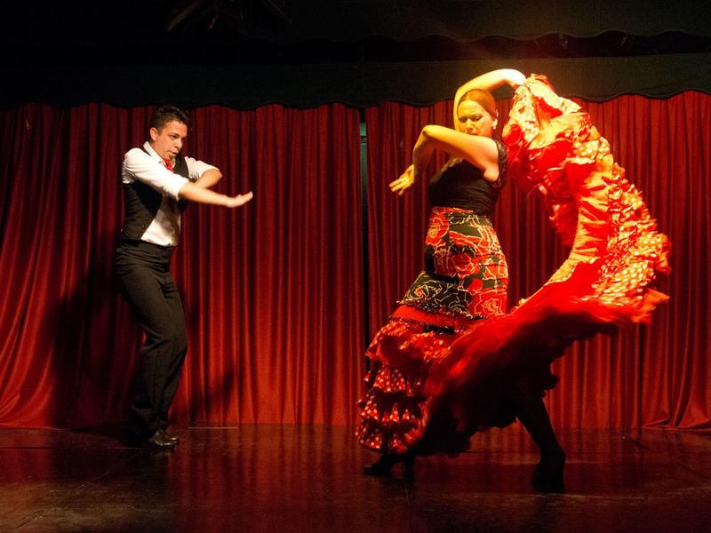 Un homme et une femme exécutent une danse flamenco devant un rideau rouge.