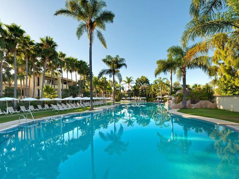 Grand piscine extérieure avec chaises longues et palmiers dans une station balnéaire ensoleillée.