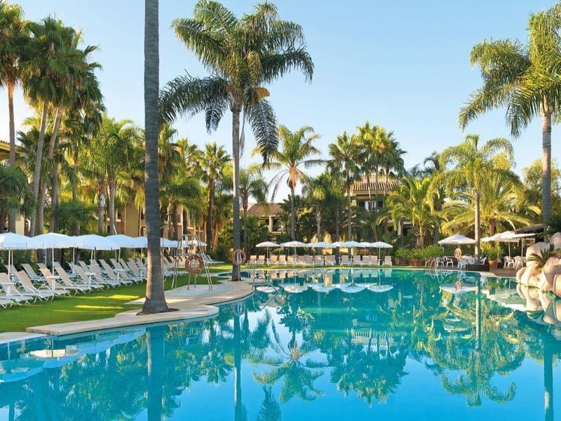 Grand piscine avec chaises longues et palmiers dans une station balnéaire tropicale.