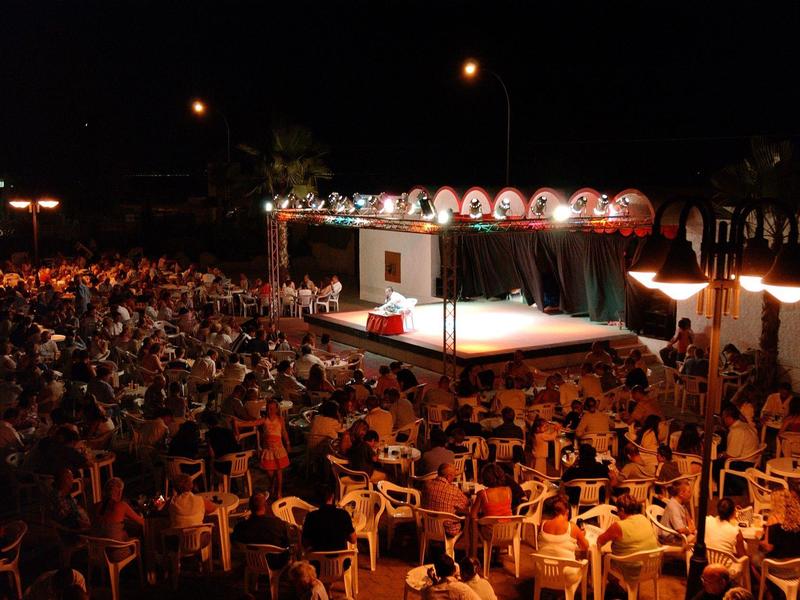 Large crowd seated in front of an illuminated stage at night.