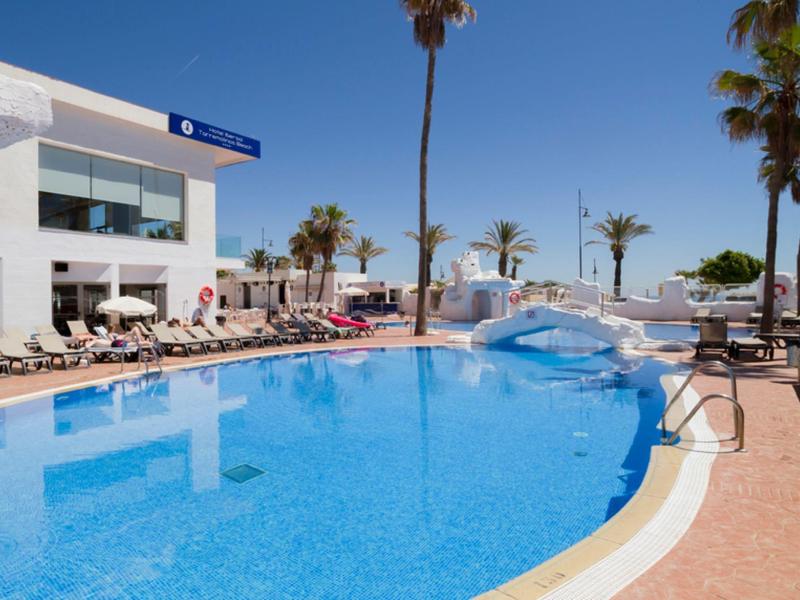Outdoor pool with bridge, sun loungers, and palm trees under clear sky