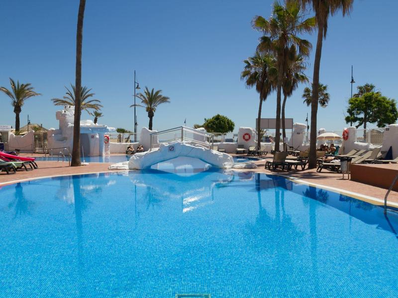 Clear blue swimming pool with palm trees and sun loungers at a sunny hotel resort.