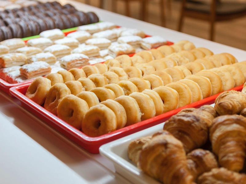 Various baked goods like donuts, croissants, and cookies on trays at a buffet.