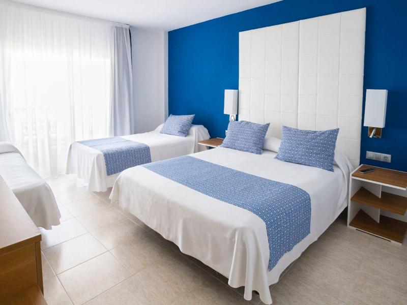 Brightly furnished hotel room with two beds and blue accents on walls and bedding.