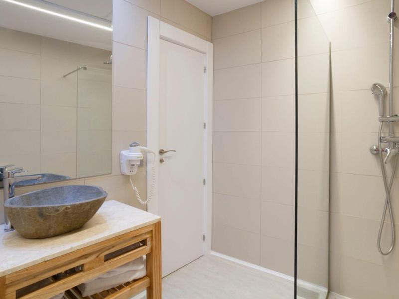 Modern bathroom with sink, wooden cabinet, shower, and white door.