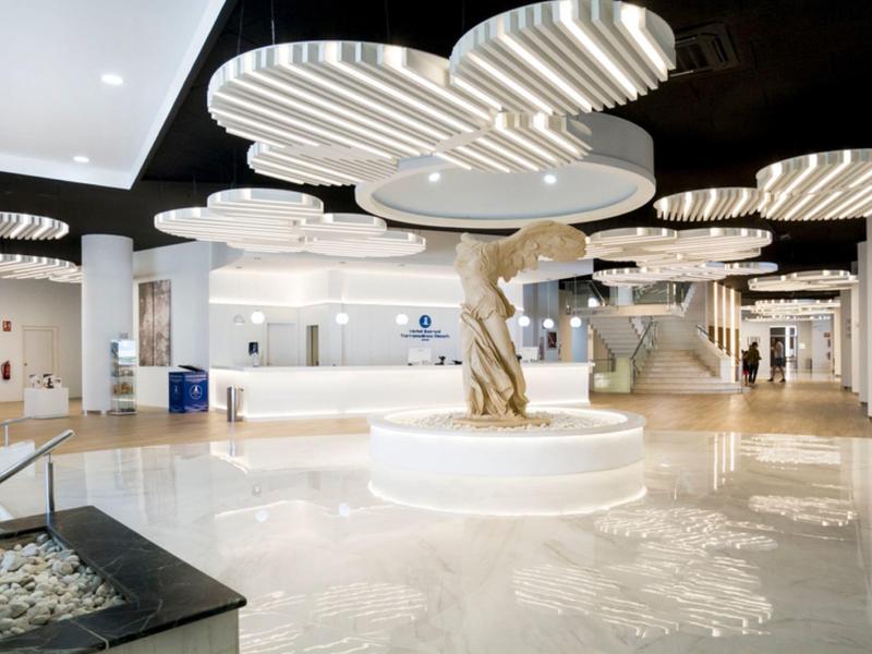 Bright, modern hotel lobby area with round illuminated ceiling features and a central sculpture.