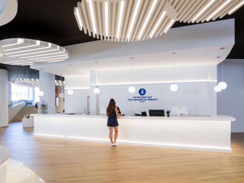 Modern hotel reception with light wood flooring and a woman at the illuminated front desk.