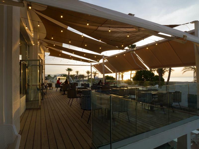 Hotel terrace with chairs and tables under large sunshades in the evening.