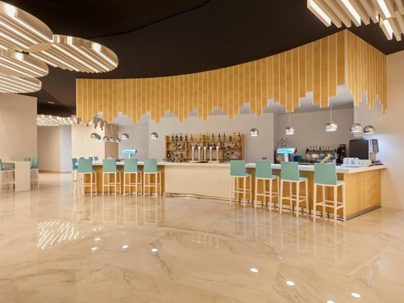 Modern bar area with blue padded bar stools and decorative wooden ceiling element.