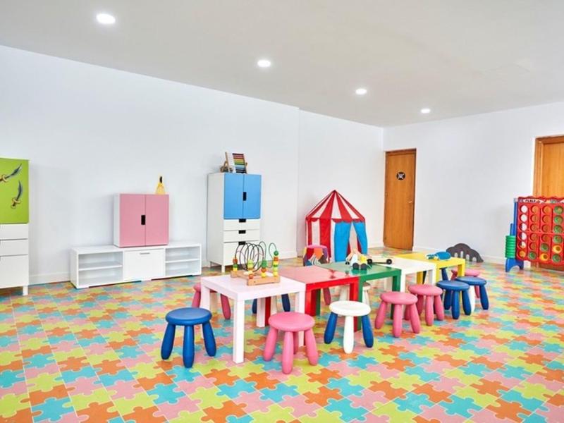 Colorful children’s playroom with small tables, stools, and toys in a bright space.