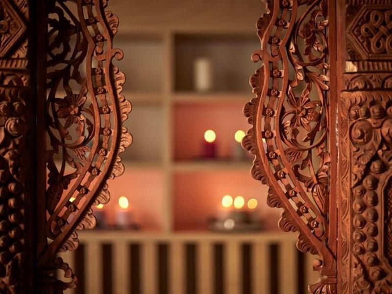Ornate carved wooden doors open to a room softly lit by warm candlelight.