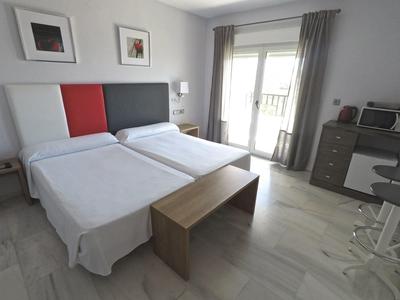 Camera d'hotel moderna con due letti singoli, panca in legno e balcone.