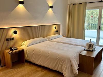 Camera d'hotel moderna con due letti singoli, mobili in legno e balcone con porta scorrevole in vetro.