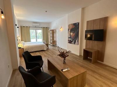 Camera d'hotel moderna con letto, poltrone, mobili in legno e finestra grande.