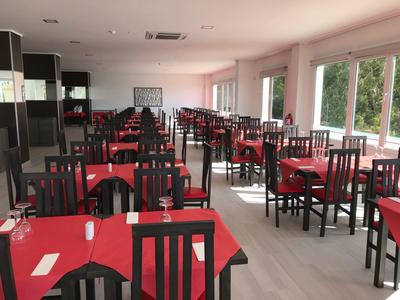 Ampia sala da pranzo con tavoli e sedie, tovaglie rosse e bicchieri apparecchiati.