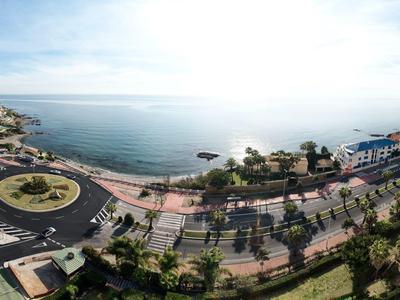 Vista panoramica di una strada costiera con una rotonda, palme e mare sullo sfondo.