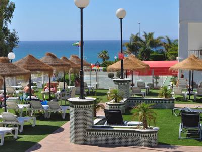 Area giardino verde con lettini, ombrelloni di paglia e vista sul mare blu.