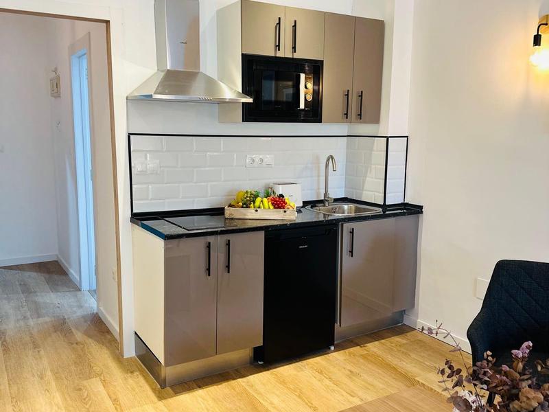 Cucina moderna con ante in legno, lavandino nero, microonde e parquet chiaro