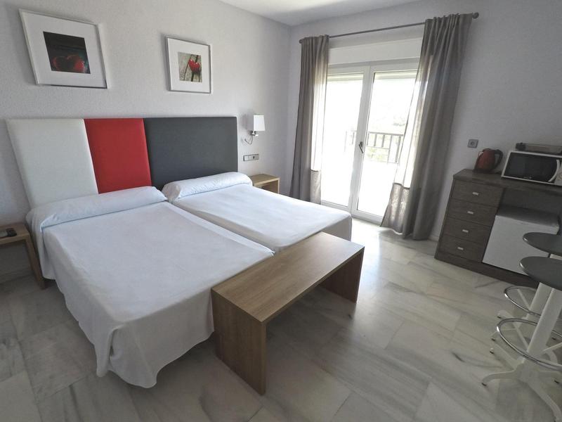 Camera d'hotel moderna con due letti singoli, panca in legno e balcone.