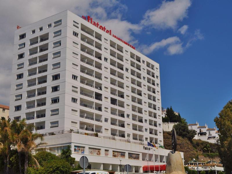 Edificio di hotel bianco a più piani con stanze con balcone sotto un cielo azzurro.