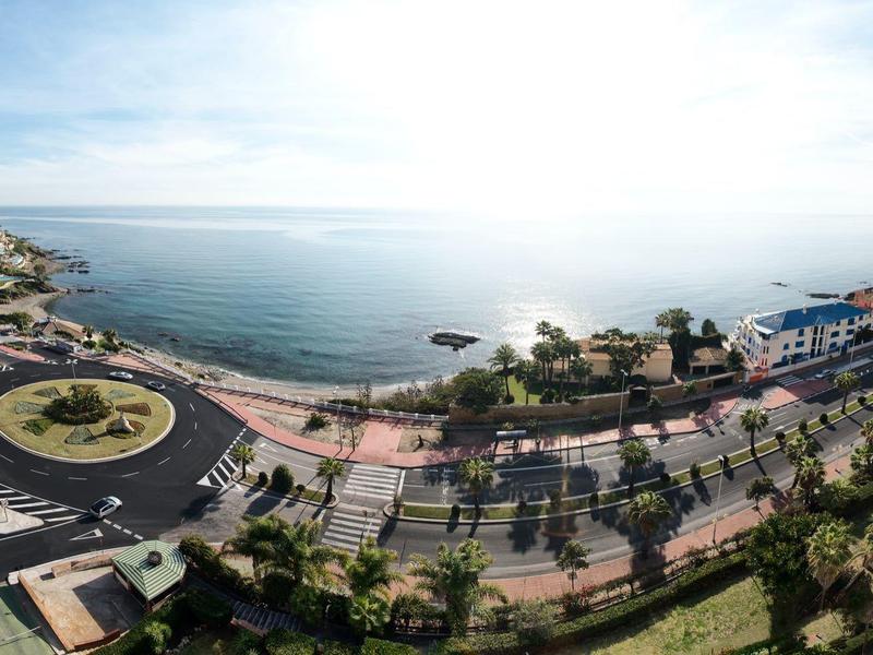 Vista panoramica di una strada costiera con una rotonda, palme e mare sullo sfondo.