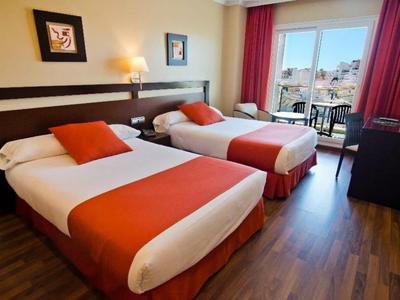 Chambre d'hôtel avec deux lits, literie rouge, sol en bois et vue sur le balcon