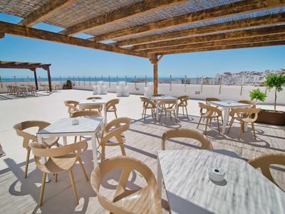 Terrasse couverte avec tables et chaises, vue sur la ville et la mer en arrière-plan.