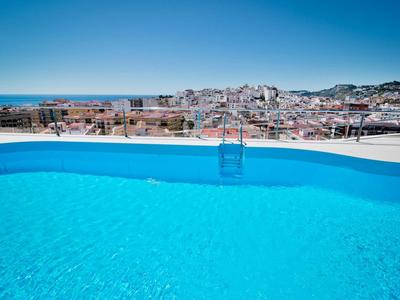 Piscine bleue claire avec vue sur la ville et la mer en arrière-plan sous un ciel ensoleillé.