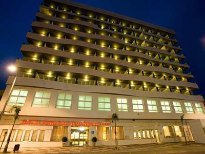 Hochhaus mit vielen beleuchteten Balkonen und großer Glasfront bei Nacht.