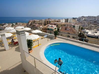 Terrasse sur le toit avec piscine ronde, espaces assis et vue sur la ville et la mer sous un ciel clair.