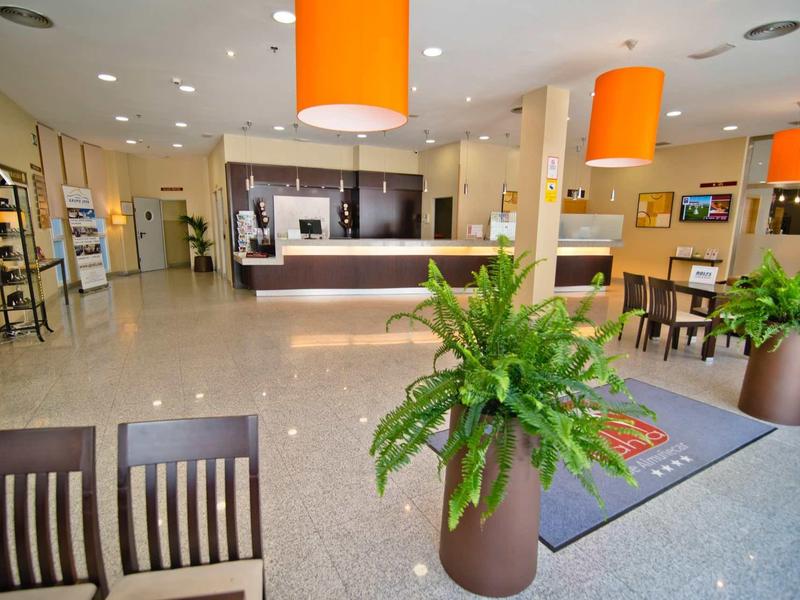 Hall d'hôtel lumineux avec réception, plantes et lampes orange.