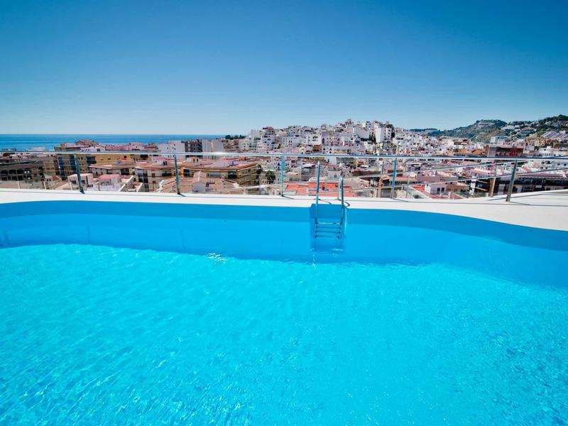 Une piscine bleue claire avec vue sur une ville et la mer en arrière-plan.