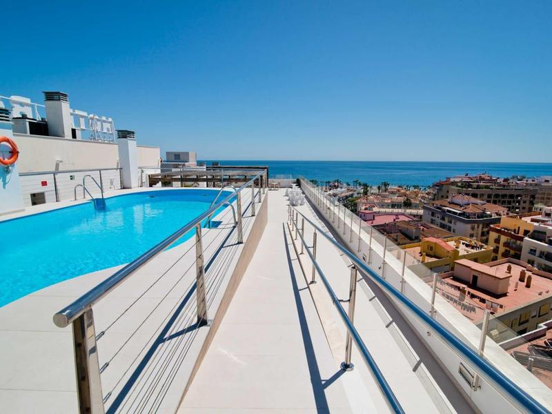 Piscine moderne sur le toit avec vue sur la ville et la mer sous un ciel clair.