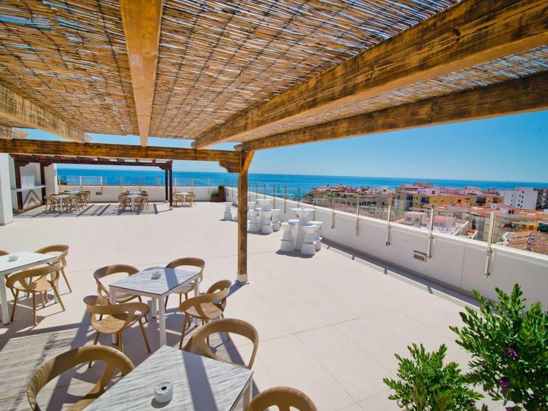 Terrasse sur le toit avec sièges sous un auvent en bois et vue sur la mer par une journée ensoleillée.