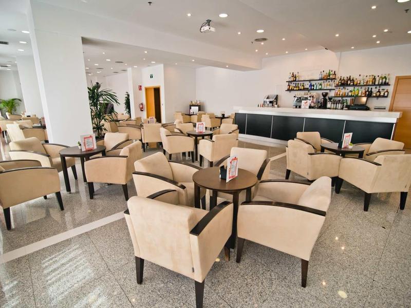 Espace lounge d'hôtel moderne avec fauteuils beiges et petites tables.