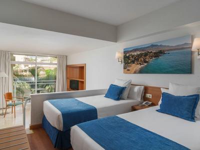 Bright hotel room with two beds, blue accents, sea view, and modern furnishings.