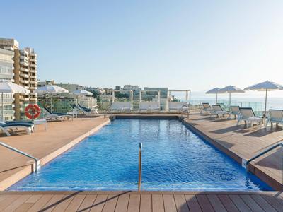 Outdoor hotel pool with sun loungers and umbrellas under clear blue sky.
