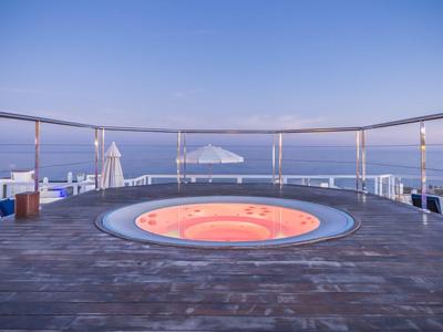 Outdoor jacuzzi on wooden deck with ocean view under clear sky at sunset