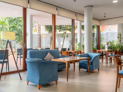 Modern seating area with blue armchairs and wooden tables by large glass windows.