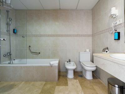 Modern bathroom with bathtub, toilet, bidet, large mirror, and beige tiles.