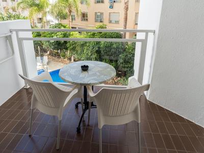 Balcony with two white chairs and a round marble table, overlooking greenery and a pool.
