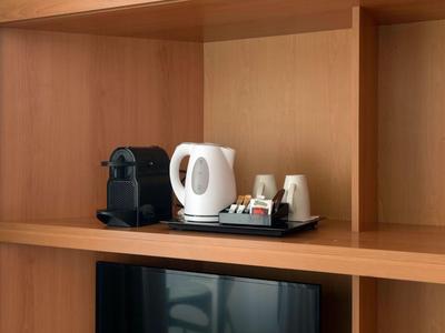 Coffee machine, electric kettle, cups, and tea setup on wooden shelf above TV.